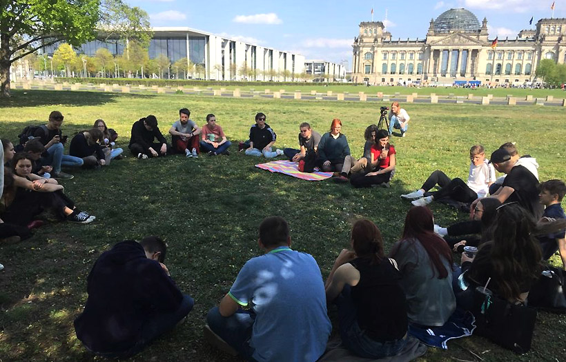 Eine Schülergruppe sitzte auf einer Wiese in Berlin. Im Hintergrund ist der Reichstag zu erkennen.