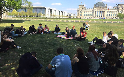 Schülergruppe sitzt auf einer Wiese in Berlin. Im Hintergrund ist der Reichstag zu erkennen.